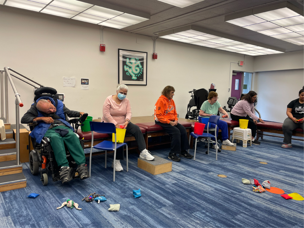 Group of people placing bean bags off the floor into a bucket in Daily Living Skills Class